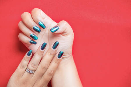 Closeup of beautiful groomed woman's hands with green spring summer nail design on red background....
