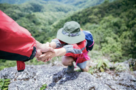 Person hike friends helping each other up a mountain. Man and woman giving a helping hand and active fit lifestyle. Asia couple hiking help each other. concept of friendship, teamwork.の写真素材