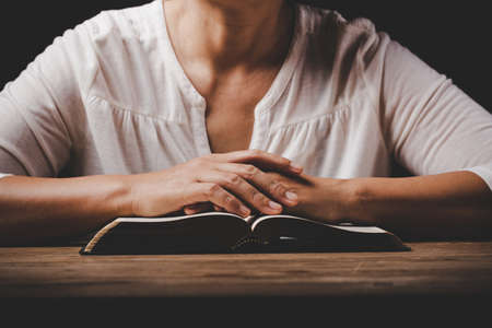 Close up of christian woman hand on holy bible are pray and worship for thank god in church with black background, adult female person are reading book, concept for faith, spirituality and religionの写真素材