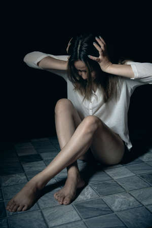 Young person woman sad, stress and loneliness sitting in dark room, Unhappy and crying teenage girl from domestic violence, An adult female expresses feelings of despair, anxiety from harassment.の写真素材