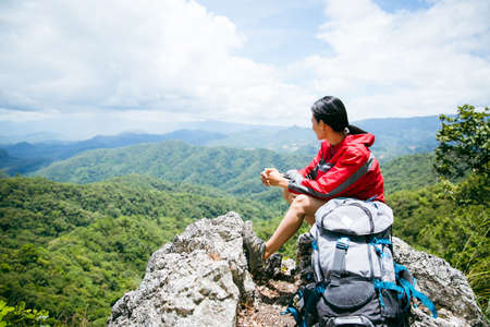 Young person hiking female sitting on top rock, Backpack woman looking at beautiful mountain valley at sunlight in summer, Landscape with sport girl, high hills, forest, sky. Travel and tourism.の写真素材