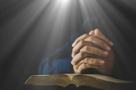 Hand folded in prayer to god on Holy Bible book in church concept for faith, spirituality and...