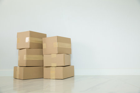 Stack of cardboard boxes for moving, Empty room with a white wall and cardboard boxes with unbranded barcode on the floor. Delivery of goods, shopping. Cardboard boxes on gray wall background.の写真素材