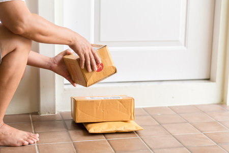 Woman collects parcel at door. box near door on floor. Online shopping, boxes delivered to your front door. Easy to steal when nobody is home. Parcel in cardboard box on doorstep. Delivery serviceの写真素材