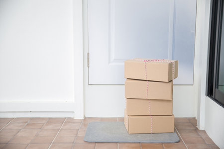 Cardboard parcel box near door on floor. Online shopping, boxes delivered to your front door. Easy to steal when nobody is home. Parcel in cardboard box on doorstep. Delivery serviceの写真素材