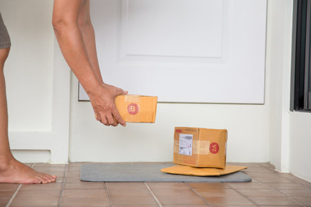 Woman collects parcel at door. box near door on floor. Online shopping, boxes delivered to your front door. Easy to steal when nobody is home. Parcel in cardboard box on doorstep. Delivery serviceの写真素材