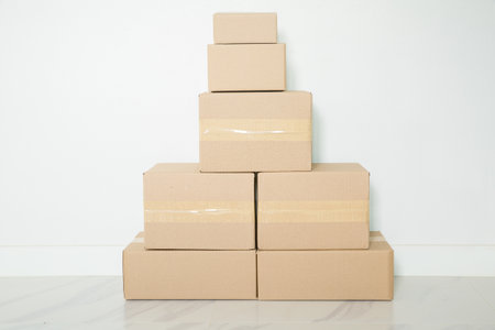 Stack of cardboard boxes for moving, Empty room with a white wall and cardboard boxes with unbranded barcode on the floor. Delivery of goods, shopping. Cardboard boxes on gray wall background.の写真素材