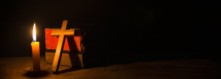 Light candle with holy bible and cross or crucifix on old wooden background in church.Candlelight and open book on vintage wood table christianity study and reading in home.Concept of christ religionの写真素材