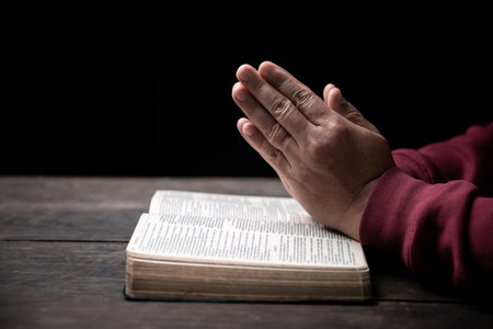 Hands folded in prayer on a Holy Bible in church concept for faith, spirituality and religion, man...