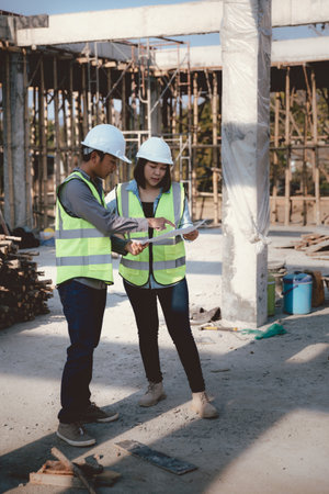 Two specialists inspect commercial, Industrial building construction site. Real estate project with civil engineer, designing commercial buildings on paper. Skyscraper concrete formwork frames.の写真素材