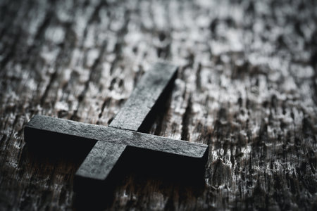 A wooden Christian cross crucifix on a grunge board background. Wooden Christian cross on grey table against blurred lights, space for text.の写真素材