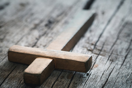 A wooden Christian cross crucifix on a grunge board background. Wooden Christian cross on grey table against blurred lights, space for text.の写真素材