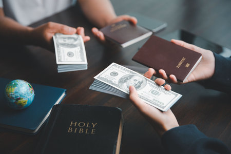 Concept of Christian ministry. Small groups pray together for Christian mission. Mission to spread gospel and religion of Christianity around world. Hands holding dollar and passport on wooden table.の写真素材