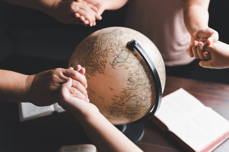 Christian group praying for globe and people around the world on wooden table with bible. Christian small group holding hands and praying together around a wooden table with bible page in homeroom.の写真素材