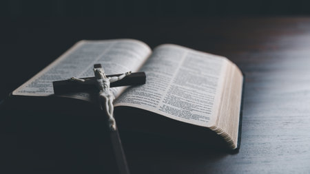 Wooden Christian cross crucifix on open holy bible background. Wooden Christian cross on grey table against blurred lights, space for text.の写真素材