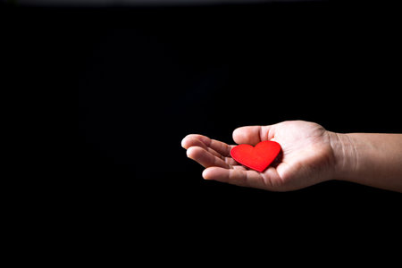 The red heart is on hand that showing love to another person. Heart is the symbol of showing love, cares, charity, help and compassion. People in the families and communities love each other.の写真素材