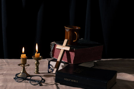 Step back in time with this vintage still life capturing the essence of spirituality. An old book, the Holy Bible, rests alongside a crucifix and a lit candle on a rustic wooden table.の写真素材