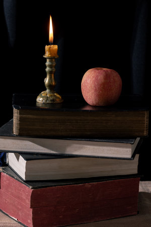 Vintage Still Life: Illuminated Wisdom and Tranquility with an Old Book, Bible, and Candle on a Wooden Table. Nostalgic Serenity and Faith through an Old Book, Bible, Candle, and Apple.の写真素材