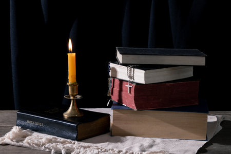 Step back in time with this vintage still life capturing the essence of spirituality. An old book, the Holy Bible, rests alongside a crucifix and a lit candle on a rustic wooden table.の写真素材