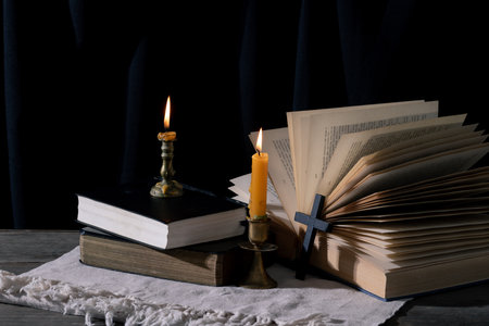 Step back in time with this vintage still life capturing the essence of spirituality. An old book, the Holy Bible, rests alongside a crucifix and a lit candle on a rustic wooden table.の写真素材