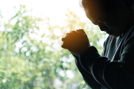 Woman prays by a window, embracing devotion and reflecting on her spiritual beliefs. The gentle light and tranquil ambiance create an atmosphere of serenity and introspection.の写真素材