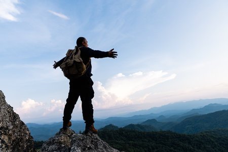 Male tourist on top of rocky mountain. A peaceful man meditating yoga relaxing alone standing and spreading arms on a mountain top at sunrise with nature landscape.の写真素材
