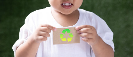 Cute little Asian boy holding a brown recycled paper card with recycling sign. Reuse reduce recycle...