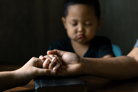 Christian family praying together concept. Child and mother worship God in home. Woman and boy hands praying to god with the bible begging for forgiveness and believe in goodness.の写真素材
