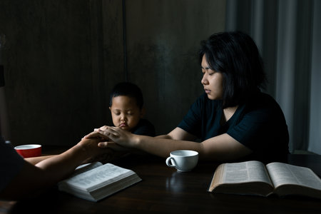 Christian family praying together concept. Child and mother worship God in home. Woman and boy hands praying to god with the bible begging for forgiveness and believe in goodness.の写真素材
