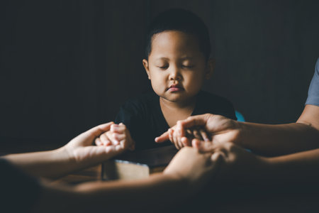 Christian family praying together concept. Child and mother worship God in home. Woman and boy hands praying to god with the bible begging for forgiveness and believe in goodness.の写真素材