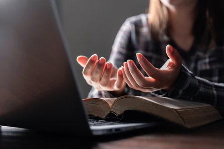 Christian online technology concept. Hands praying of christian with digital computer laptop, Online live church for sunday service. Asian catholic man are reading Holy bible book and online study.の写真素材