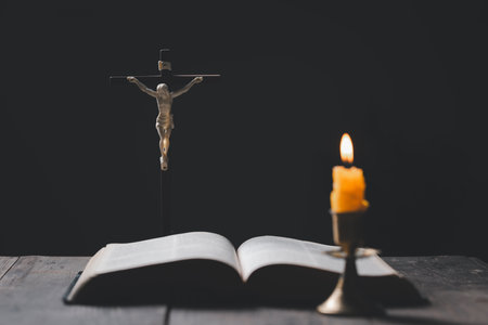 Light candle with holy bible and cross or crucifix on old wooden background in church.Candlelight and open book on vintage wood table christianity study and reading in home.Concept of christ religionの写真素材