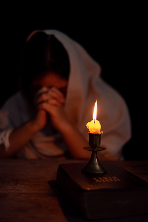 Candle light with blur young girl praying in dark night background. Woman person worship God with faith and belief. religion, christian prayer concept. Christian teenage girl and faith.の写真素材