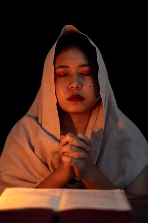 Young girl with candle light praying in dark night background. Woman person worship God with faith and belief. religion, christian prayer concept. Christian teenage girl and faith.の写真素材