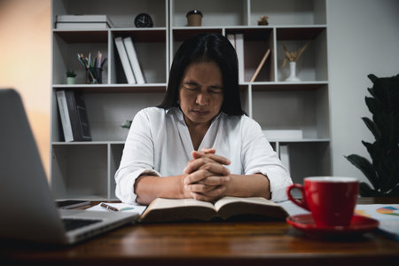 Businesswoman Praying with Eyes Closed. Businesswoman with her hands folded waiting for good news sitting at workplace at the table in the office. Hands folded in prayer gesture beg about something.の写真素材