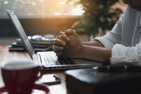 Businesswoman Praying with Eyes Closed. Businesswoman with her hands folded waiting for good news sitting at workplace at the table in the office. Hands folded in prayer gesture beg about something.の写真素材