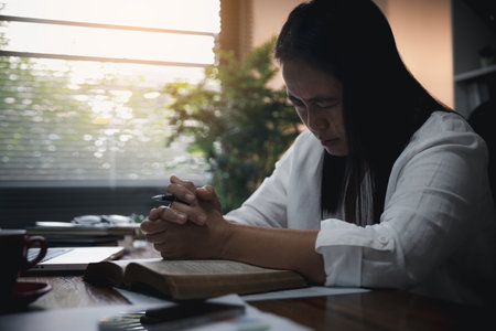 Businesswoman Praying with Eyes Closed. Businesswoman with her hands folded waiting for good news sitting at workplace at the table in the office. Hands folded in prayer gesture beg about something.の写真素材