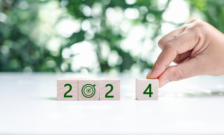 2024 numbers and earth care symbol on circle eco wooden blocks on wood table, green leaves background. Happy new year 2024 with the world care. Green environmental sustainability concepts.の写真素材
