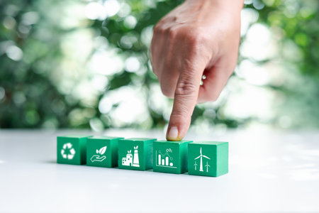 Hand put green wooden cubes with net zero icon and white icon on bokeh nature. Net zero and carbon...