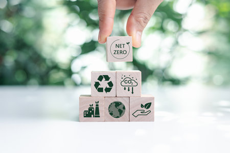 Hand put wooden cubes with green net zero icon and green icon on bokeh nature. Net zero and carbon neutral concept. Net zero greenhouse gas emissions target. Climate neutral long term strategy.の写真素材