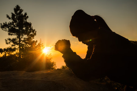 Silhouette of woman kneeling down praying for worship God at sky background. Christians pray to jesus christ for calmness. In morning people got to a quiet place and prayed. copy space.の写真素材