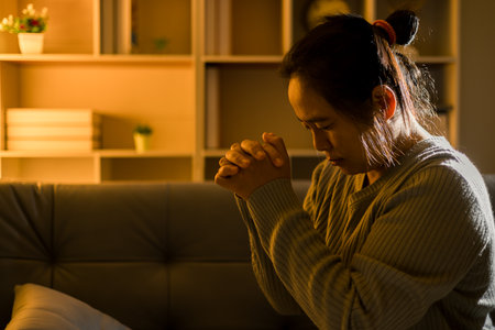 Christian religious woman praying at night sitting on couch in living dark room at home. Human...