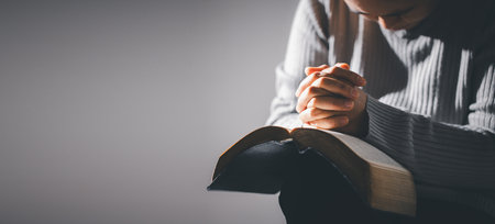 Hands folded in prayer on holy bible in church concept for faith, spirituality and religion....