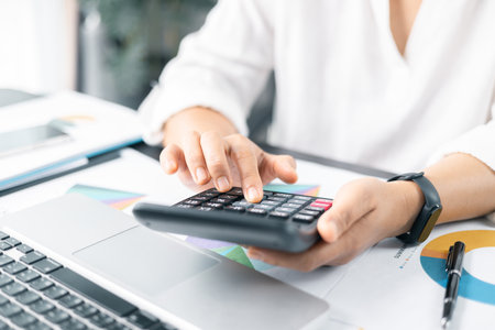 Businesswoman hand doing finances and calculate on desk about cost at home office. Business financing accounting banking concept. Woman working on desk with using calculator, finance accounting.の写真素材