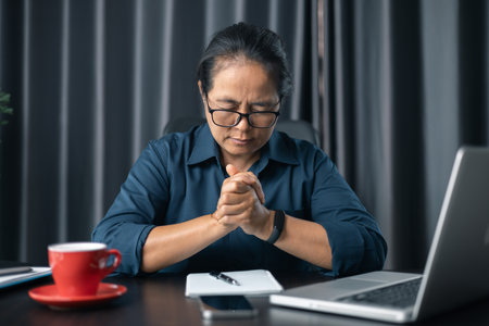 Contemplative prayer thinking in office. Businesswoman praying at work. Hands folded in prayer gesture beg about something. woman with hands clasped praying while sitting at desk in office.の写真素材