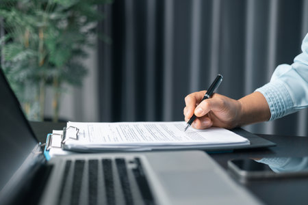 Close up businesswoman signing documents. Hand of woman write business document charts at office desk. Woman signing document, focus on female hand holding pen, putting signature at official paper.の写真素材