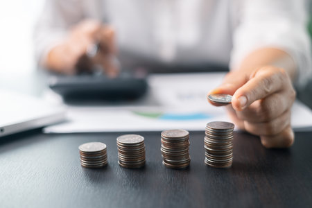 Human hand stacking coins over office background. Concept of investment management and portfolio diversification. Business diagram on financial report with coins.の写真素材
