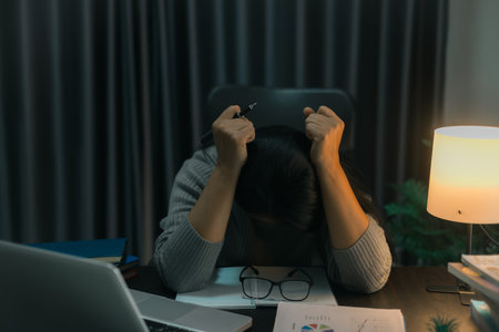 Depression at work. Asian Businesswoman sitting and working hard at with front of computer and lots of documents on table in workplace at late with serious action, Work hard and too late conceptの写真素材