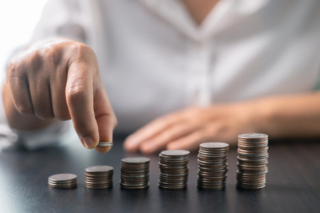 Human hand stacking coins over office background. Concept of investment management and portfolio diversification. Business diagram on financial report with coins.の写真素材