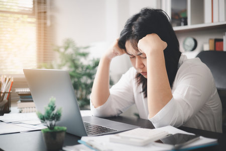 Stressed businesswoman, dealing with the pressures of work and the weight of depression, finds herself struggling in the office, feeling sleepy and overwhelmed by the demands of her job.の写真素材
